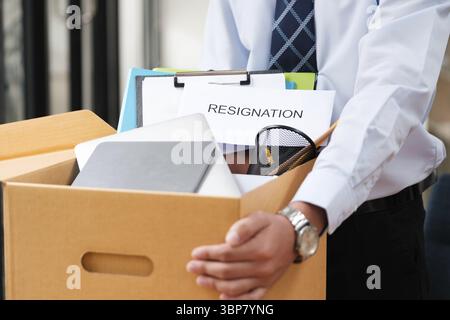 Dipendente maschio che imballa i suoi effetti personali in una scatola di cartone con una lettera di dimissioni, segnalando la sua decisione di abbandonare il lavoro Foto Stock