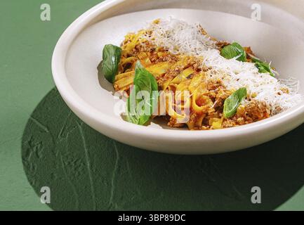 Cibo, Una porzione di pappardelle è condita con salsa di carne salata, formaggio grattugiato e foglie di basilico fresco. Il piatto è presentato su un colore chiaro Foto Stock