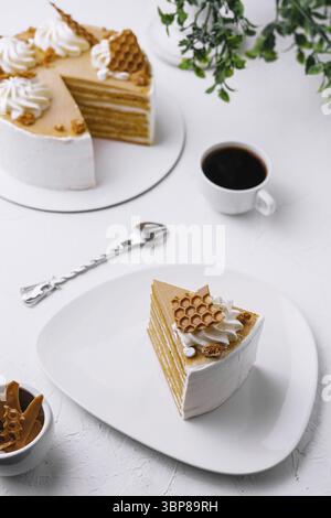 Cibo, fette di torta a strati di miele su un piatto accanto a una torta completa e una tazza di caffè, con una presentazione elegante Foto Stock