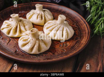 Cibo, gnocchi tradizionali georgiani, khinkali, serviti su un piatto di legno intagliato con erbe fresche Foto Stock