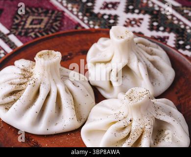 Cibo, tre gnocchi di khinkali georgiani serviti su un piatto di argilla su una tovaglia a motivi etnici Foto Stock