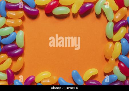 Jelly Beans assortiti bordo con copyspace su sfondo arancione Foto Stock