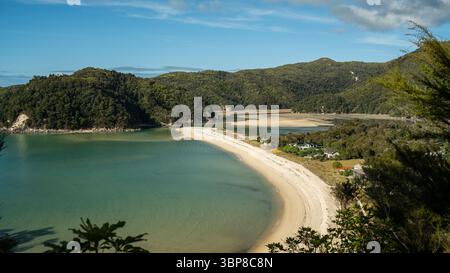 Uno splendido panorama costiero rivela una baia turchese incorniciata da colline verdeggianti sotto un cielo limpido. La composizione utilizza linee iniziali e la regola di Foto Stock