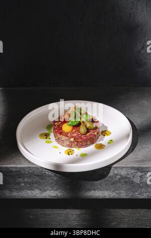 Cibo, Una tartare di manzo splendidamente presentata viene servita su un piatto bianco, caratterizzato da coloratissimi cornici e gocciolatoi. Il piatto è appoggiato su un'elegante scura Foto Stock