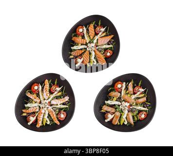 Cibo, tre insalate su piatti ovali neri con salmone, gamberi, avocado e lattuga, splendidamente disposte e scattate dall'alto su sfondo bianco Foto Stock