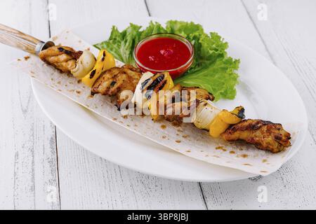 Cibo: Lo shish kebab di pollo alla griglia viene servito su pane pita con salsa di pomodoro, cipolla e peperone su un piatto bianco Foto Stock