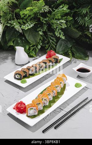 Cibo, due piatti di sushi colorati con ripieno di salmone e granchio, guarniti con wasabi e zenzero sottaceto, adagiati su un lussureggiante fogliame verde Foto Stock