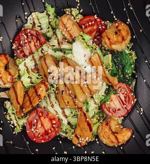 Cibo, deliziosa insalata con gamberetti alla griglia, capesante scottate, salmone e verdure serviti su un piatto nero Foto Stock
