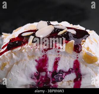 Cibo, elegante dessert pavlova con composta di bacche, mandorle a fette e zucchero a velo da vicino Foto Stock
