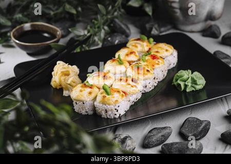 Cibo, sushi al forno con formaggio su un piatto nero servito con salsa di soia, zenzero sottaceto e wasabi Foto Stock