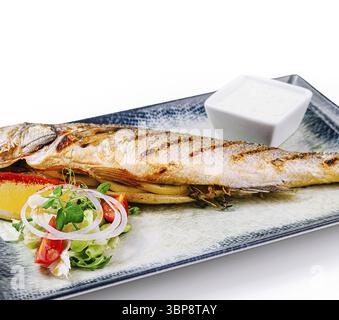 Cibo: Branzino alla griglia servito su un piatto con insalata fresca, limone, erbe aromatiche e salsa bianca Foto Stock