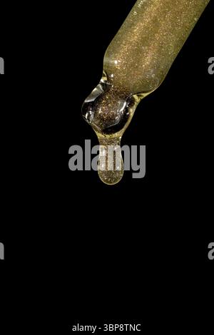Pipetta in vetro con siero facciale con caduta su sfondo nero. Prodotto cosmetico liquido per la cura della pelle con primo piano luccicante. Goccioline di olio essenziale m. Foto Stock
