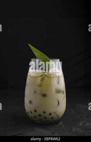 Cibo, bicchiere di latte matcha ghiacciato con perle di tapioca è guarnito con una foglia di palma, creando una bevanda rinfrescante ed esotica Foto Stock
