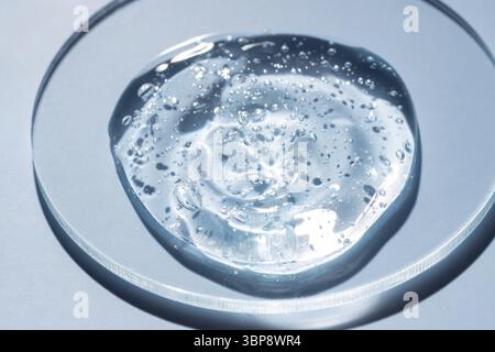 Goccia o sbavatura di cosmetici. Goccia di gel trasparente liquido con bolle su sfondo blu su piastra Petri Foto Stock