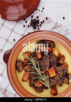 Cibo, delizioso stufato di manzo con polenta e verdure in un piatto rustico di terracotta, guarnito con rosmarino Foto Stock