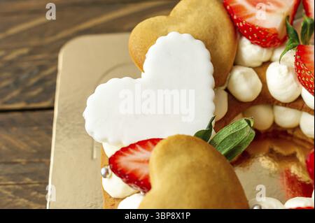 Pan di Spagna con fragole, barrette di cioccolato al latte rosa, spruzzi d'argento, crema di vaniglia e biscotti di crema al cuore da vicino. Dolce estivo per bi Foto Stock