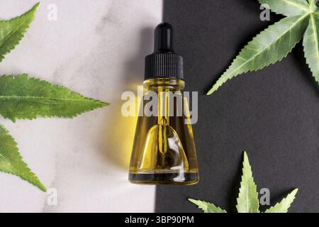 Vista dall'alto del concetto di contagocce di olio o siero con superficie di Cannabis. Cosmetica naturale. Olio CBD, tintura THC e foglie di canapa su un doppio marmo e nero backgroun Foto Stock