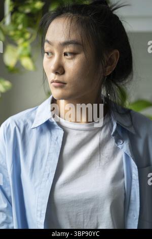 Infelice triste giovane donna asiatica che guarda da parte, sente disperazione, depressa donna pessimista a casa in piedi a casa pensando alla vita quotidiana pro Foto Stock