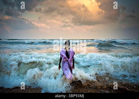 Una giovane donna indiana si erge sul surf in una spiaggia durante il tramonto. Foto Stock