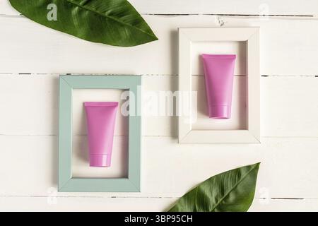 Set di cosmetici per la cura della pelle viso, corpo o mani. Tubi cosmetici bianchi rosa in cornici luminose su sfondo di legno. Concetto di bellezza cosmetica creativa. Foto Stock