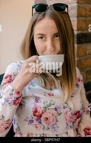 Donna in camicetta floreale che beve il tè sorridente Foto Stock