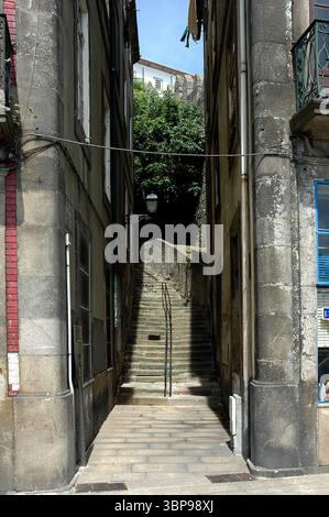 Un vicolo stretto con una scala che porta verso l'alto, fiancheggiata da vecchi edifici in pietra. Il vicolo e' bagnato dalla luce del sole, con una lanterna appesa in alto. Foto Stock