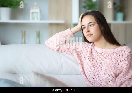 Una donna in salotto guarda lontano seduto su un divano di casa Foto Stock