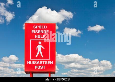 Cartello stradale con il testo olandese per "cure Emercengy" e "medico di famiglia/centro medico di famiglia" di fronte a un cielo blu Foto Stock