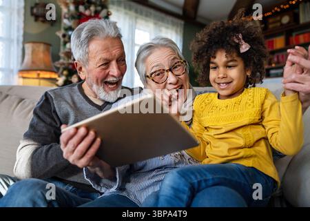 Felice coppia di anziani che utilizza un moderno computer portatile con gadget tecnologico insieme al nipote a casa. Foto Stock