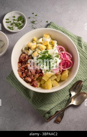Insalata di patate all'uovo con pancetta ed erbe fresche in un piatto Foto Stock