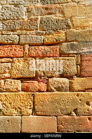 Antiche pareti di mattoni in calde tonalità di sabbia giallo-arancione illuminate dalla luce del sole con forme di mattoni irregolari Foto Stock