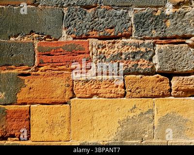 Antiche pareti di mattoni in calde tonalità di sabbia giallo-arancione illuminate dalla luce del sole con forme di mattoni irregolari Foto Stock