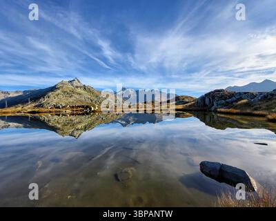 Lago di montagna mozzafiato riflesso alla calda luce del sole mattutino con panorama montano e nuvole di velo sul passo di Grimsel, Alpi svizzere Foto Stock