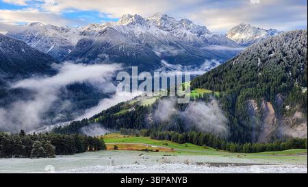 Paesaggio montano unico con montagne innevate nelle Alpi svizzere, ciuffi di nebbia e prati verdi e foresta verde in un'atmosfera mistica Foto Stock