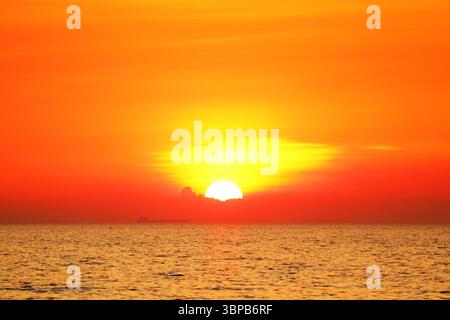 Splendido sole luminoso che sorge sul vibrante cielo arancione sopra il mare calmo Foto Stock
