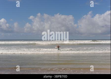 : Surfer con una tavola da surf sulla spiaggia di sabbia di Weligama sulla costa meridionale dell'isola dello Sri Lanka entrando nell'Oceano Indiano con onde alte in una giornata di sole Foto Stock