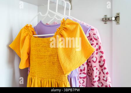 Vista ravvicinata di vestiti per bambini dai colori vivaci su appendiabiti in un armadio bianco Foto Stock