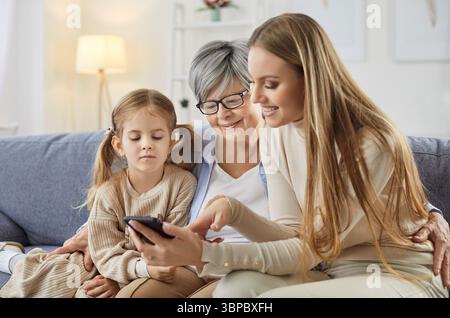Figlia e nipote che insegnano a madre anziana o nonna come utilizzare lo smartphone Foto Stock