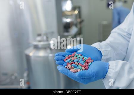 I guanti tengono le pillole assortite in un moderno impianto farmaceutico, evidenziando la produzione avanzata di farmaci e la sicurezza Foto Stock