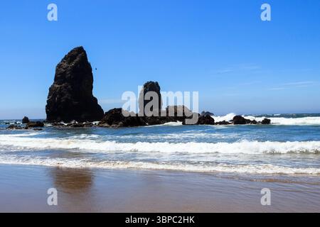Cannon Beach, Oregon - 26 giugno 2016: Le onde si infrangono attorno all'iconica Haystack Rock e ad altre formazioni rocciose. Foto Stock