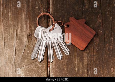 Chiavi di casa in metallo con portachiavi in legno a forma di casa su un tavolo da giardino con agenti atmosferici. Primo piano Foto Stock