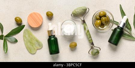 Prodotti cosmetici naturali con estratto di oliva e strumenti per massaggi su sfondo chiaro Foto Stock