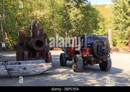 Campo 18, Seaside, Oregon, USA - 2 settembre 2017: Una Jeep Wrangler si erge accanto ad un vecchio pezzo arrugginito di attrezzature per il taglialegna. Foto Stock