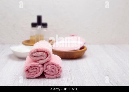 Una pila di asciugamani rosa in bagno con shampoo, balsamo e sapone, offrendo spazio libero per la messaggistica dei prodotti. Foto Stock