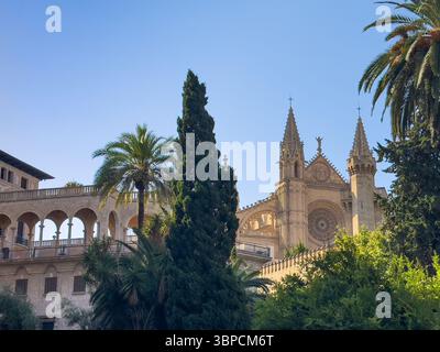 Palma di Maiorca, Spagna - 12 luglio 2024: Palazzo dell'Almudaina e torri della cattedrale viste da Placa de la Reina. Parcheggiare di fronte Foto Stock