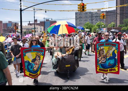 Una vivace scena della sfilata delle Sirene di Coney Island presenta partecipanti che portano striscioni raffiguranti una Sirenetta della Regina e il Re Nettuno, accanto a una donna in una Foto Stock