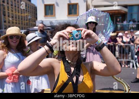 Una giovane donna con i capelli scuri, che indossa una parte superiore gialla della senape e tiene una piccola macchina fotografica colorata agli occhi, è la messa a fuoco centrale. E' circondata da Foto Stock