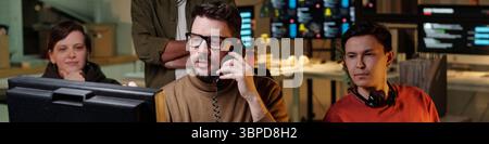 Gruppo di uomini e donne di etnie diverse che lavorano al call center truffa, utilizzando computer e cuffie, concentrandosi su monitor e conversazioni telefoniche Foto Stock