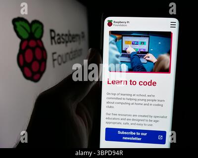 In questa illustrazione fotografica, una persona ha in mano uno smartphone con la pagina Web dell'organizzazione di computer Raspberry Pi Foundation sullo schermo davanti al logo. Foto Stock