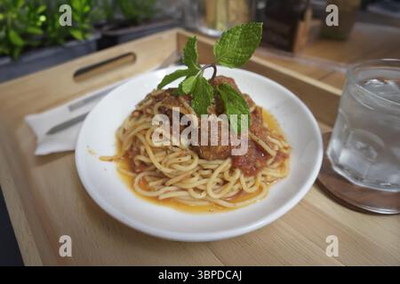 spaghetti con polpette serviti su un rustico tavolo di legno su una soleggiata terrazza a bordo piscina. Goditi un pasto perfetto all'aperto con una vista rinfrescante. Questo vi Foto Stock